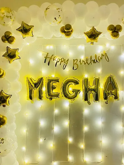 A simple and elegant birthday backdrop in white and gold, with a personalized name banner for "Megha".