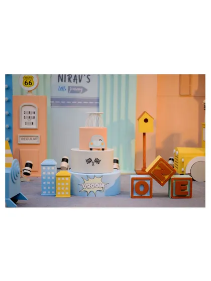 Another view of the vehicle-themed cake and prop setup, showing the 'Vroom' and 'Boom' comic-style signs.