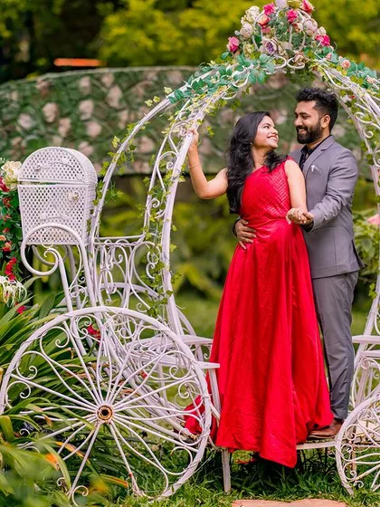 A sweet moment between a couple in a Cinderella carriage. The bride's red dress and the lush garden setting make for a classic and romantic pre-wedding photo.