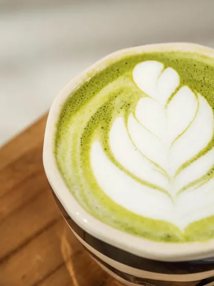 A slightly wider view of the matcha latte art, showing the full heart-shaped leaf design. The bright, clean lighting is ideal for a cafe menu or social media feed.