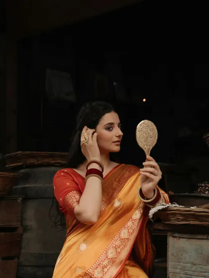 A candid moment of adjustment, this portrait captures the model arranging her hair while looking in the mirror, adding a touch of realism to the traditional scene.