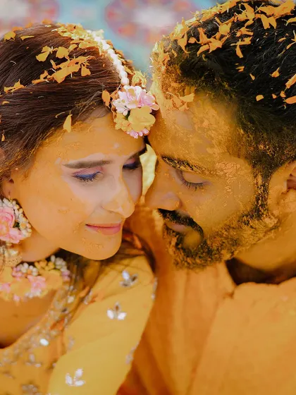 An intimate close-up of the couple during their haldi, covered in turmeric and flower petals.