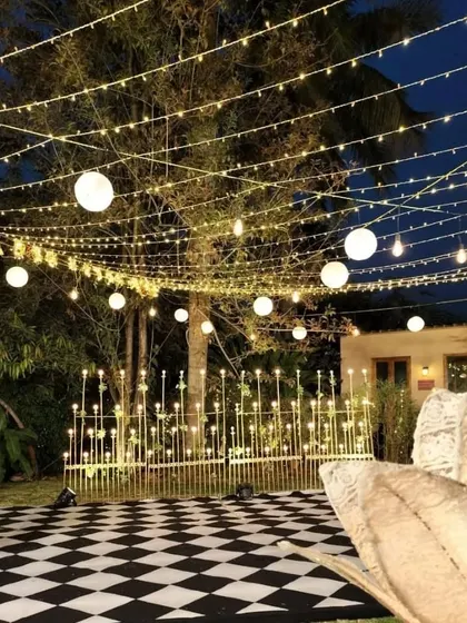 A stylish Sangeet setup with a checkered dance floor, surrounded by modern candle-like floor lamps and topped with a canopy of string lights and lanterns for a magical evening.