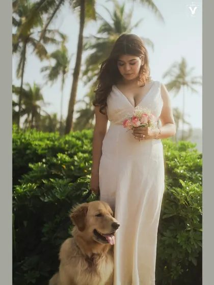 A lovely portrait of the bride holding a bouquet, standing next to her calm golden retriever against a backdrop of palm trees. This image beautifully includes the pet as a key part of the pre-wedding celebration.