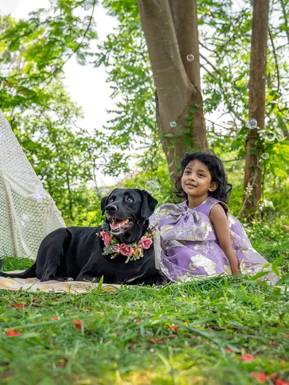 A magical portrait of a little girl and her black Labrador sitting together in a park, surrounded by bubbles.