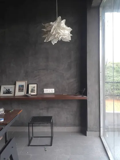 A quiet corner in our Ghitorni studio, where a simple wooden shelf floats on a textured grey wall. This minimalist composition of material, light, and form reflects our core design principles.