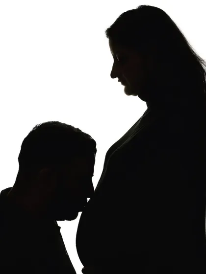 A simple yet powerful silhouette portrait. The dad-to-be kneels to kiss the baby bump, creating a beautiful and symbolic image of his love for both mother and child.