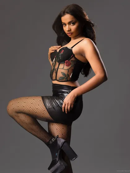 A model in a sheer floral embroidered corset, faux leather skirt, and platform heels. This look is perfect for a lingerie or alternative fashion brand's catalogue.