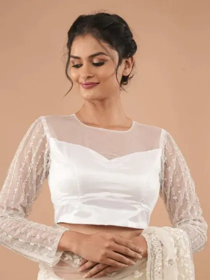This white blouse features a sheer yoke and long sleeves, all embellished with sparkling sequins.