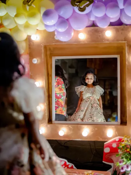 A little guest looking in a vanity mirror with lights at the butterfly garden party, capturing a moment of childhood wonder.
