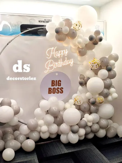 We created this modern photo backdrop for a boss's birthday celebration. The setup features a sophisticated palette of white and grey balloons on a metal ring frame, a custom 'BIG BOSS' sign, and a warm 'Happy Birthday' neon light to complete the look.