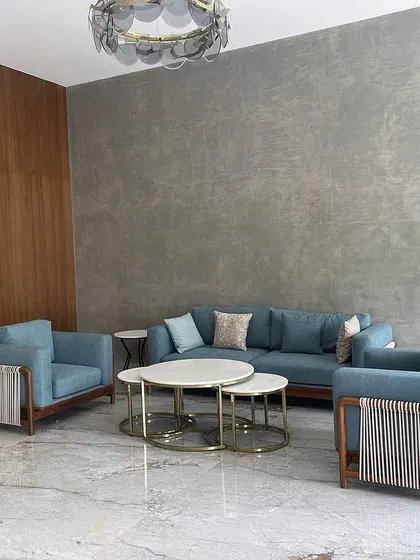 A living room set from the same Tiripur project, featuring a sofa and armchairs with unique woven rope detailing on the arms, paired with a nested set of marble-topped coffee tables.