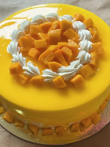 A top view of our seasonal Mango Cake, decorated with fresh mangoes and whipped cream swirls.