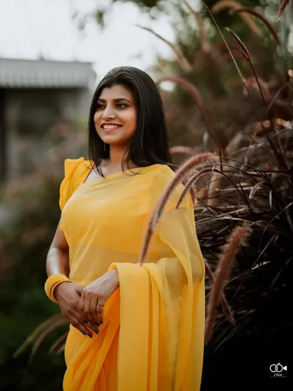 A beautiful solo portrait of the bride in her yellow saree, smiling serenely amidst tall, feathery grass.