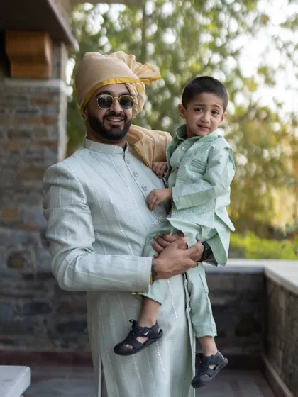 A heartwarming photo of the groom in a mint green sherwani, holding a young boy dressed in a matching outfit.
