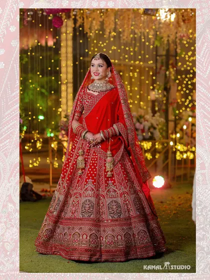 A full-length portrait of the bride in her stunning red lehenga, set against a backdrop of fairy lights.