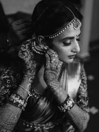 An intimate black and white shot of the bride getting ready. The focus on her hands adjusting her earring, with the intricate mehndi, creates a timeless and elegant image.