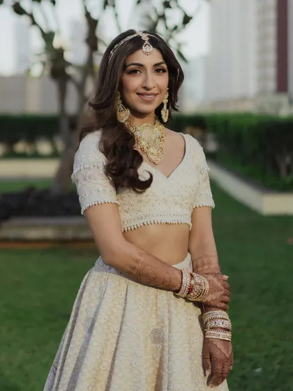 Sheena's soft golden hour bridal look. Her ivory lehenga and gold jewelry are paired with a luminous base, subtly defined eyes, and a muted nude lip for a look of understated luxury.