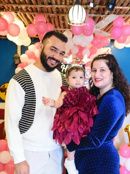 A happy family of three posing at their daughter's birthday party, surrounded by pink balloons.