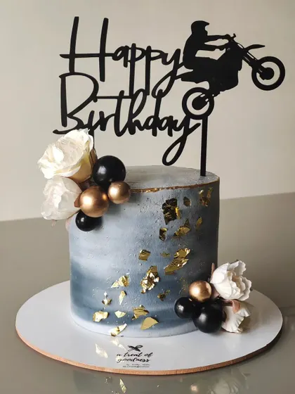 This cake was designed for a bike lover, featuring a cool concrete-effect buttercream with scattered gold leaf. A bold black acrylic topper and simple floral accents complete this modern, edgy look.