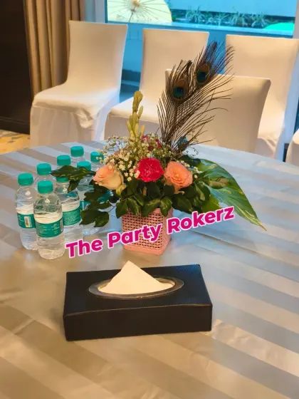 A simple table centerpiece for a Teej party, made with roses and peacock feathers to match the event's theme.