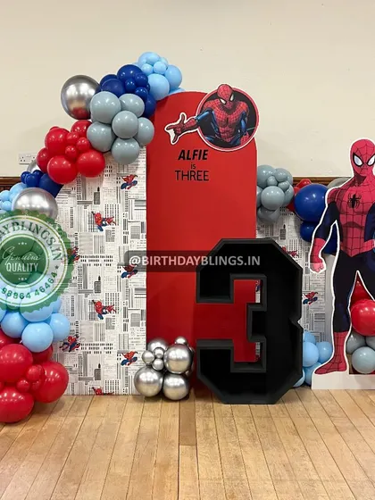 This Spider-Man theme for a third birthday features a life-sized character cutout and a backdrop combining a comic-print panel with a solid red panel. The custom-built number '3' adds a personal touch.