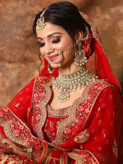 A beautiful shot of a bride with her eyes closed, showcasing the warm, coppery-gold eyeshadow that complements her red lehenga.
