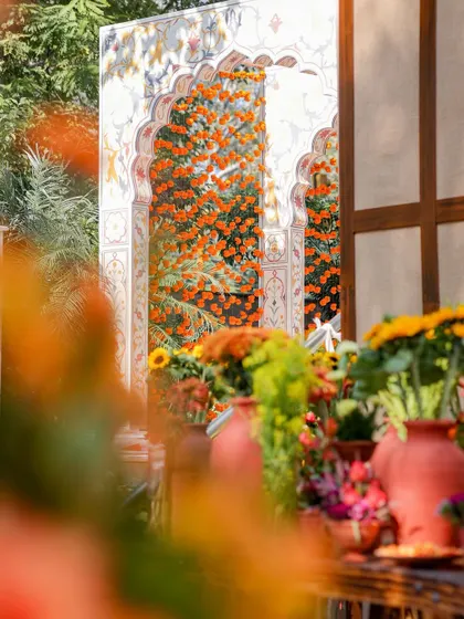 An artfully composed shot showing the layers of the decor. In the foreground, terracotta pots with colorful flowers, and in the background, the grand hand-painted archway adorned with marigolds.