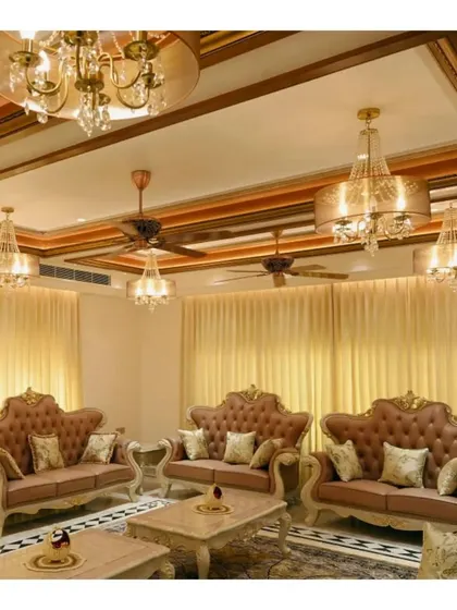 A formal living room that combines classic European-style furniture with traditional Indian design elements. The coffered ceiling with wood trim and multiple chandeliers creates a warm, luxurious, and inviting atmosphere for entertaining.