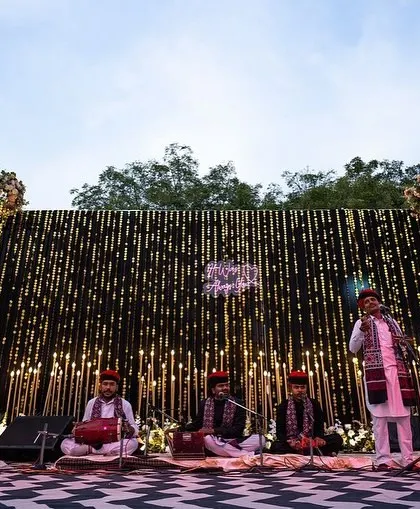 The stage for a folk music performance at a pre-wedding event, featuring a backdrop of hanging lights that create a warm and inviting atmosphere.