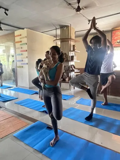 A student holds tree pose while cradling a puppy, perfectly capturing the blend of focus and fun in these special classes.