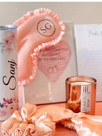 A collection of bridal essentials. This set includes a personalized floral tumbler, a satin eye mask and scrunchie, a "Bride's To-Do List" notepad, and a rose-scented candle.