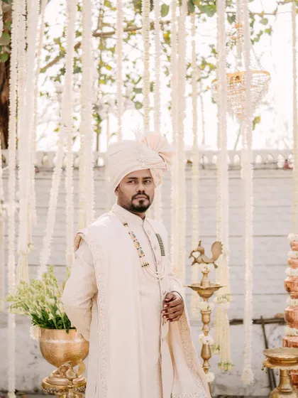 A classic portrait of the groom in his off-white sherwani, standing in front of the beautiful floral decor of his wedding.