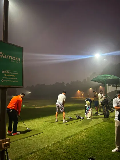 Two golfers practice side by side under the lights on a foggy night.