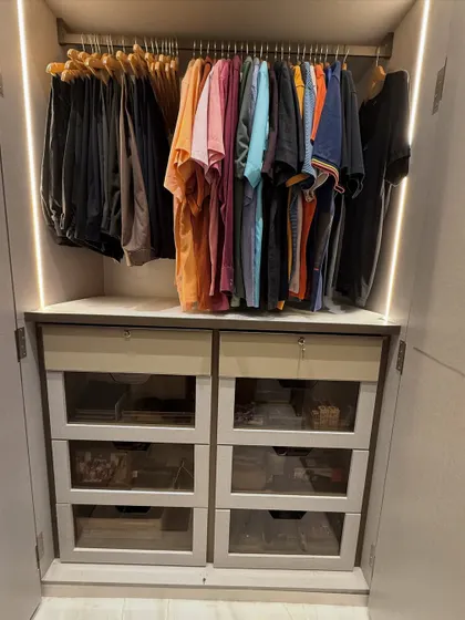 A compact but mighty wardrobe section. Colorful t-shirts are hung above a bank of drawers with glass fronts, offering a mix of visible and concealed storage.