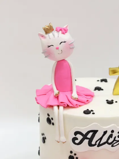 A chic and adorable kitty cake topper. This figurine features a princess cat in a pink tutu and a tiny gold crown, sitting on a cake dotted with paw prints.