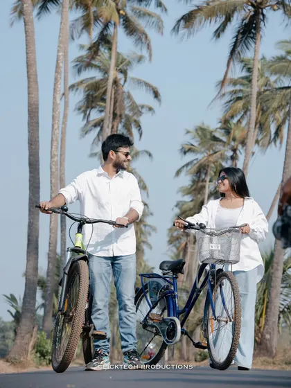 A couple stands with their bicycles on a road lined with palm trees in Goa, a perfect shot for a casual and scenic pre-wedding album.