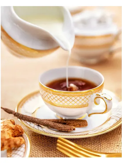 Milk is elegantly poured into a cup of tea, set in a classic, high-end tea service. This food photography captures a moment of action with a sense of luxury and comfort.