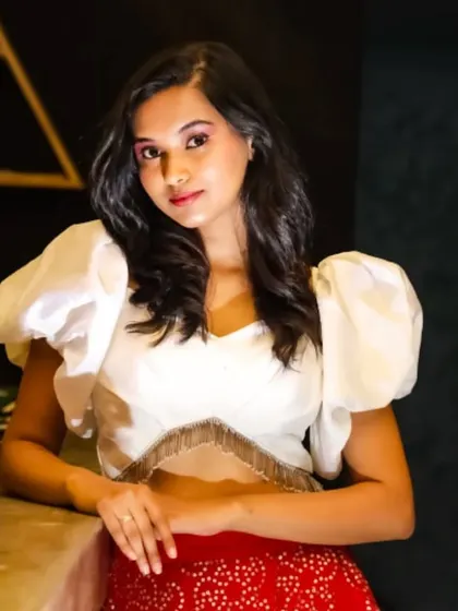 A model wearing a modern Indo-Western lehenga with a red brocade skirt and a white crop top with dramatic puff sleeves. A great option for a sangeet or party.