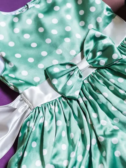 A lovely mint green polka dot satin dress. The design is completed with a crisp white satin sash that ties into a large, elegant bow.
