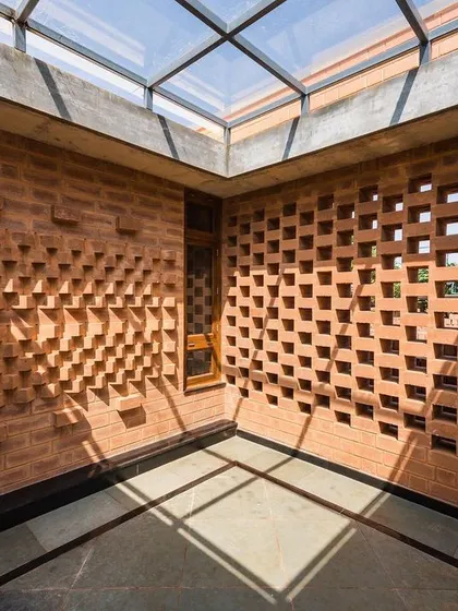 In this office space, a combination of a textured brick wall and a perforated jaali wall interact with light from a skylight, creating a rich tapestry of light, shadow, and texture.