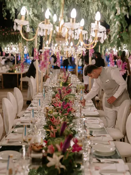 The finale dinner for K+G was planned to perfection. This long table setting features mirrored surfaces reflecting hanging floral arrangements and chandeliers, creating an immersive and glamorous dining experience.