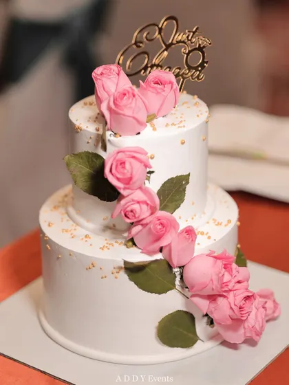 A simple yet elegant two-tiered cake adorned with a cascade of fresh pink roses and a "Just Engaged" topper. We coordinate with vendors to ensure every element, including the cake, aligns with the event's aesthetic.