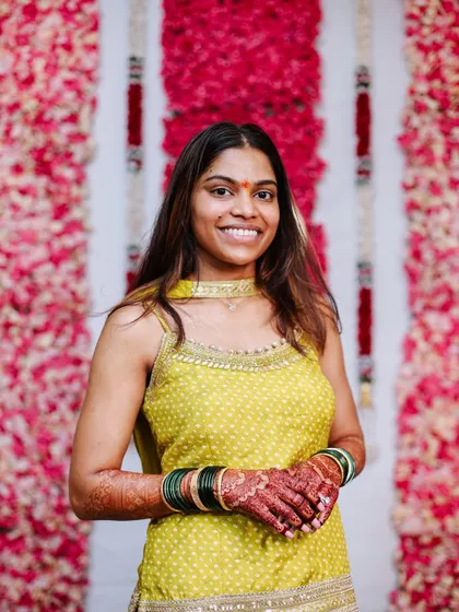 The bride smiling against a floral backdrop during her Haldi ceremony.