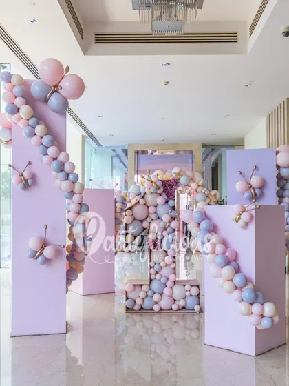 A grand entrance for a first birthday, featuring pastel purple columns decorated with balloon garlands and butterfly details.