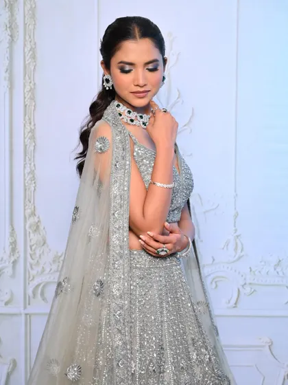 An elegant reception look in a silver lehenga with a cape, featuring a cool-toned smokey eye and a chic hairstyle.