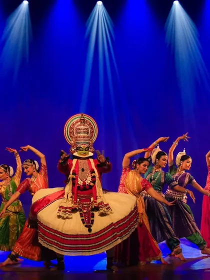 My troupe, Trikayaa Dance Foundation, performing in 'Colours of India'. The stage is lit to create a dramatic atmosphere, highlighting a central Kathakali artist surrounded by a vibrant ensemble.