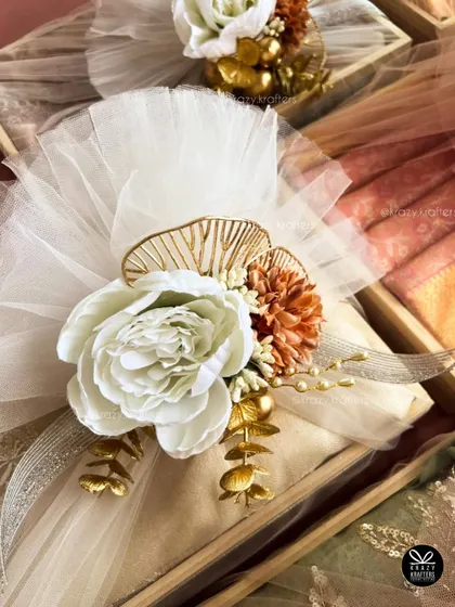 A different color palette for trousseau styling, featuring a large white peony and warm-toned flowers against white tulle. Every design is customized to the client's wedding theme.