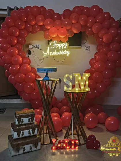 A stunning anniversary decoration with a large red heart-shaped balloon arch and a 'Happy Anniversary' neon sign.
