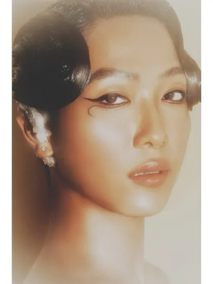 A soft, ethereal beauty close-up. The glowing light, flawless skin, and unique graphic eyeliner showcase a more artistic and delicate approach to beauty photography.